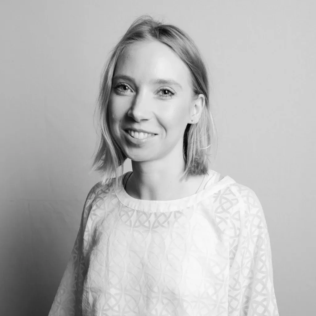 Porträt von Anette, einer Frau mit schulterlangem, hellem Haar. Sie blickt lächelnd in die Kamera und trägt ein helles, gemustertes Oberteil vor einem neutralen Hintergrund